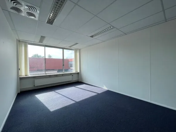 Leeg, licht kantoor met blauw tapijt aan de Jan van Eycklaan, met groot raam en systeemplafond.